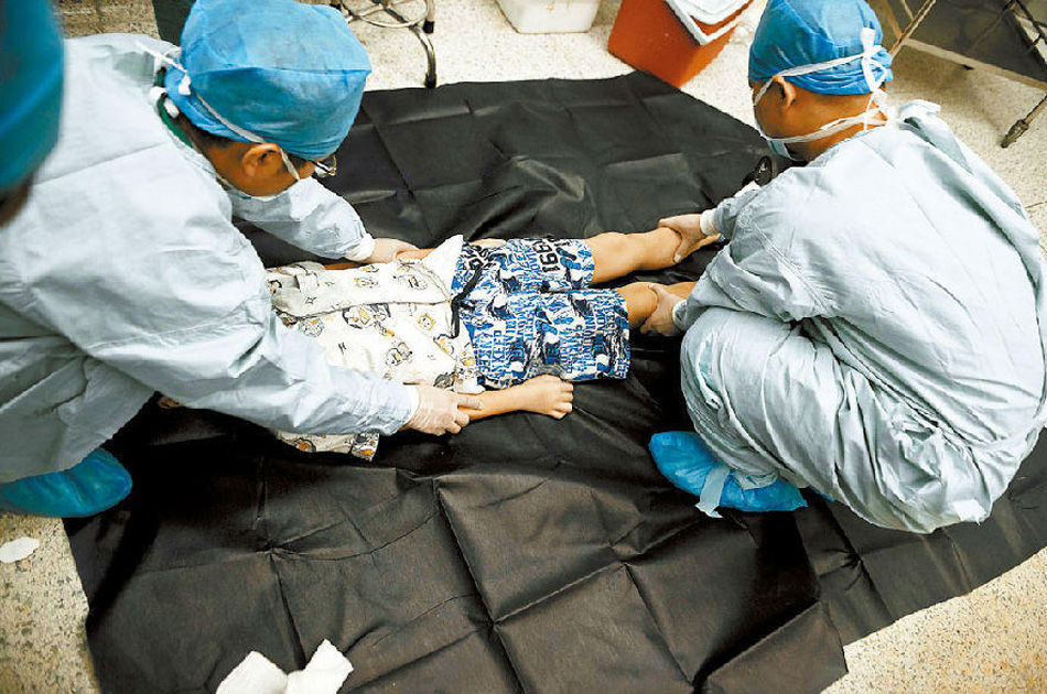 أطباء يلبسون الطفل المصاب بالورم الدماغي ملابسه، وقد تم وضع الكليتين والكبد الذي تبرع بهما في جهاز تبريد.    
