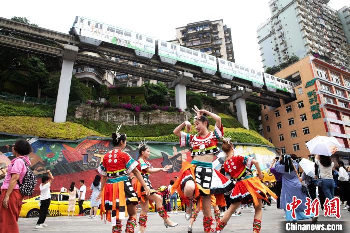  رقص فتيات قومية مياو على جانب مبنى يمر وسطه قطار تشونغتشينغ الأحادي يجذب أنظار المارة
